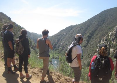 A group of students stand at the side of a dirt road, overlooking the river
